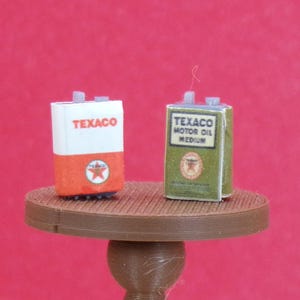 May include: Two vintage Texaco oil cans. One is red, white, and blue with the word "Texaco" printed on it. The other is green with the words "Texaco Motor Oil Medium" printed on it.