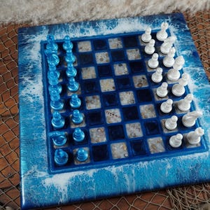May include: A square chess set with a blue and white ocean-themed design. The board features a blue and white wave pattern around the edges. The chess pieces are blue and white.