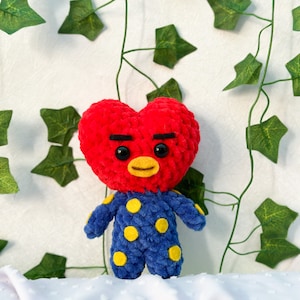 K&ouml;nnte beinhalten: Ein rotes, herzf&ouml;rmiges, geh&auml;keltes Pl&uuml;schtier mit einem blauen und gelben Outfit. Das Spielzeug hat eine schwarze Augenbraue, schwarze Augen und einen gelben Schnabel.