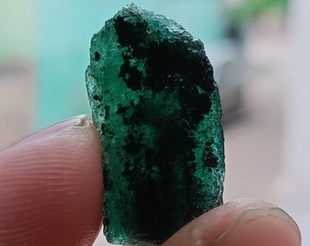 May include: A dark green, rough-cut emerald gemstone with a slightly cloudy appearance.