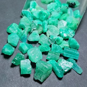 Op de afbeelding: Een verzameling ruwe smaragd edelstenen in verschillende vormen en maten. De smaragden zijn een levendige groene kleur en hebben een natuurlijke, onbewerkte afwerking.