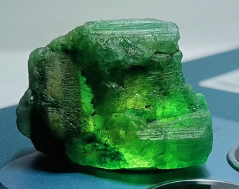 May include: A large, rough, green emerald crystal with striations and a translucent appearance.