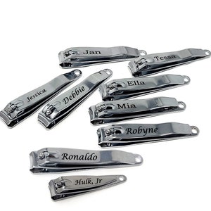 Può includere: Una collezione di tagliaunghie personalizzati in metallo argentato lucido, incisi con nomi. I nomi includono Jessica, Debbie, Jan, Tessa, Ella, Mia, Robyne, Ronaldo e Hulk, Jr.