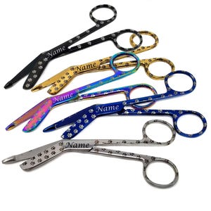 May include: A selection of pet grooming scissors in black, gold, blue, and iridescent finishes. Each scissor has a paw print design and the word "Name".