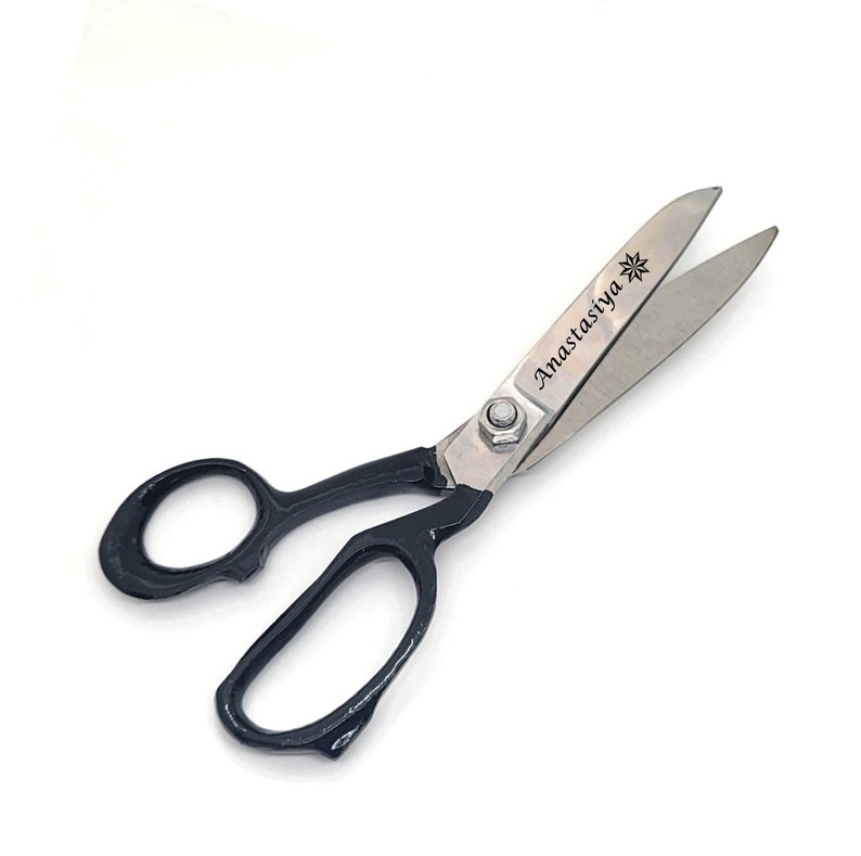 May include: Fabric shears with black handles and silver blades. The blades are engraved with the text "Anastasiya" and a star.