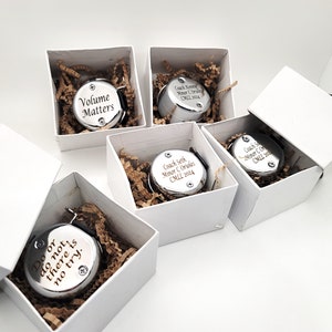 May include: Five silver round bells in white boxes with brown paper filler. The bells are engraved with different messages, including "Volume Matters", "Do or do not, there is no try", and "Coach Seth Minor C Oriales CMLL 2004".