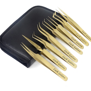 Könnte beinhalten: Satz mit zehn goldfarbenen Pinzetten mit einem schwarzen Etui. Jede Pinzette hat die Worte "Lash Galore" auf der Seite eingraviert.