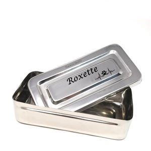 May include: A stainless steel rectangular box with a hinged lid. The lid has the name "Roxette" engraved on it, along with a paw print and a heartbeat graphic. The box is empty.