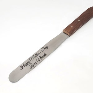 May include: A stainless steel spreading knife with a wooden handle. The blade is engraved with the text "Happy Mother's Day Love, Nicole".