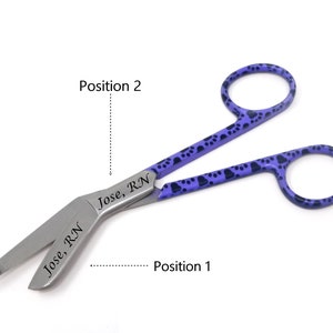 Puede incluir: Tijeras de vendaje moradas con diseño de huella de pata negra. Las tijeras están abiertas y las cuchillas están grabadas con "Jose, RN".
