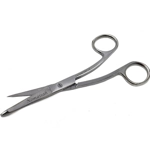 May include: Silver-colored stainless steel medical scissors featuring two finger rings and a curved blade design. The metal surface is engraved with the text "Nomaisah" on one blade and "Stainless Steel CE" near the central pivot screw.