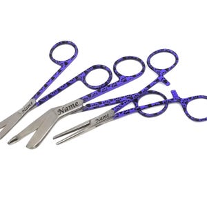 Peut inclure: Trois instruments chirurgicaux en acier inoxydable avec des poign&eacute;es violettes. Les poign&eacute;es pr&eacute;sentent un motif de pattes. Le texte "Name" est grav&eacute; sur chaque instrument. Instruments con&ccedil;us pour un usage m&eacute;dical ou v&eacute;t&eacute;rinaire.