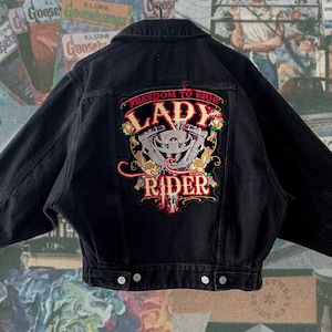 Puede incluir: Chaqueta vaquera negra con un gran parche bordado en la espalda que dice "Freedom to Ride Lady Rider" con un diseño de motor de motocicleta en el centro.