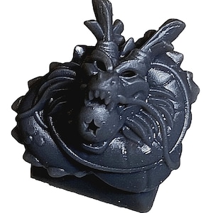 Può includere: Una testa di drago grigia stampata in 3D con una stella sul petto. Il drago ha un'espressione feroce con denti e artigli affilati.