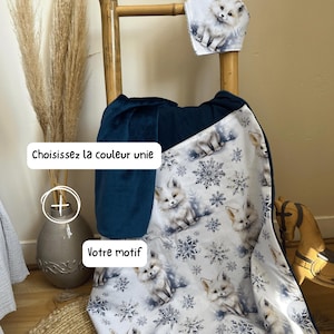 Peut inclure: Une couverture composée d'un tissu blanc à motif répété de renards arctiques et de flocons de neige bleus, associé à un tissu bleu marine uni. Le texte "Composez Votre couverture", "Choisissez la couleur unie" et "Votre motif" est visible.