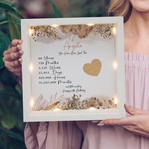May include: A white framed artwork with the text "Angela, You Have Been Loved For" and a gold heart. The artwork includes the text "60 Years, 720 Months, 3,129 Weeks, 21,915 Days, 525,960 Hours, 31,557,600 Minutes, Happy 60th Birthday."
