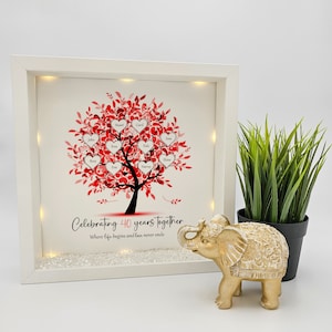 May include: A white framed illuminated picture with a red heart tree design. The tree has names written on the hearts. The text below the tree reads "Celebrating 40 years together. Where life begins and love never ends."