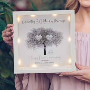 May include: A framed artwork with fairy lights, commemorating a 30th wedding anniversary. The black and white image shows a tree with two heart-shaped leaves, inscribed with "Russell" and "Donna". Text reads "Happy Pearl Anniversary" and "10,958 DAYS OF LOVE."
