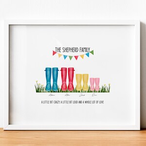 May include: A white framed print with a colorful illustration of a family of five wearing rain boots. The text reads "The Shepherd Family" with a string of colorful flags above the boots. The text below the boots reads "A little bit crazy, a little bit loud and a whole lot of love."