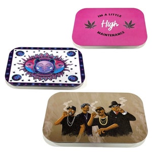 May include: Three rectangular metal rolling trays. One is pink with the text "IM A LITTLE High MAINTENANCE" and cannabis leaves. Another has a celestial design with a sun and moon. The third features a graphic of four people smoking.