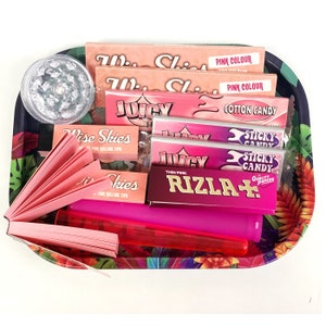 May include: A pink and white rolling tray with various rolling papers, including Wise Skies, Juicy Jay's, Rizla+, and Sticky Candy. The tray also includes a pink lighter, a grinder, and a pack of pink rolling tips.