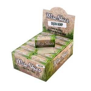 Pode incluir: Uma caixa de 24 folhas de enrolar Wise Skies Green Hemp. A caixa é marrom com detalhes verdes e apresenta uma cena de floresta. O texto "Wise Skies" está impresso em letras grandes e em negrito na parte frontal da caixa. O texto "Green Hemp" está impresso em letras menores abaixo do nome da marca. O texto "Paper on a Roll" está impresso em letras ainda menores abaixo do texto "Green Hemp".