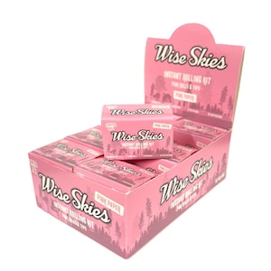 Può includere: Una scatola espositiva rosa piena di scatole rosa più piccole, ciascuna con l'etichetta "Wise Skies Instant Rolling Kit". Le scatole presentano testo e un disegno a silhouette di foresta. La scatola espositiva ha anche il logo "Wise Skies".