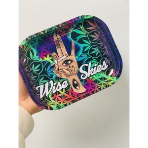 May include: A colourful metal rolling tray with a psychedelic design featuring a hand with an eye and a joint, and the text "Wise Skies".