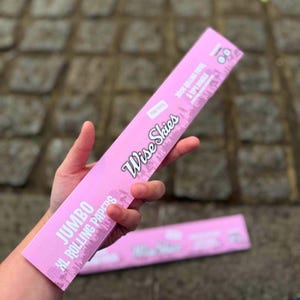 Puede incluir: Paquete rosa de papeles de liar Wise Skies Jumbo XL. El paquete tiene una escena de bosque con el texto "Wise Skies" y "Jumbo XL Rolling Papers".