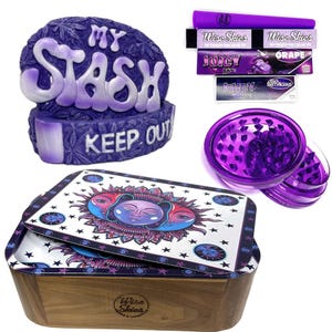 May include: Purple and white ceramic stash box with the words "My Stash" and "Keep Out".  The box is next to a purple grinder, a wooden box with a purple and white sun and moon design, and a pack of rolling papers.