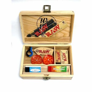 Puede incluir: Caja de madera con una variedad de accesorios para fumar, incluyendo papeles de liar, puntas de cono y un molinillo. La caja est&aacute; etiquetada como "Wise Guys" y presenta el logotipo de RAW.