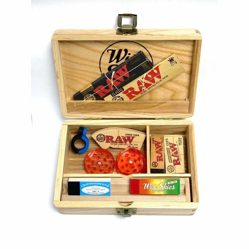Puede incluir: Caja de madera con una variedad de accesorios para fumar, incluyendo papeles de liar, puntas de cono y un molinillo. La caja est&aacute; etiquetada como "Wise Guys" y presenta el logotipo de RAW.