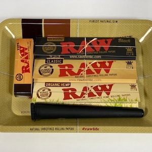 Könnte beinhalten: Eine beigefarbene Rolling Tray mit dem Text "THE NATURAL WAY TO ROLL" und "#rawlife". Das Tablett enthält eine Packung Tips, mehrere Packungen Zigarettenpapier und einen schwarzen Cone Loader. Das Zigarettenpapier ist mit "RAW" beschriftet.