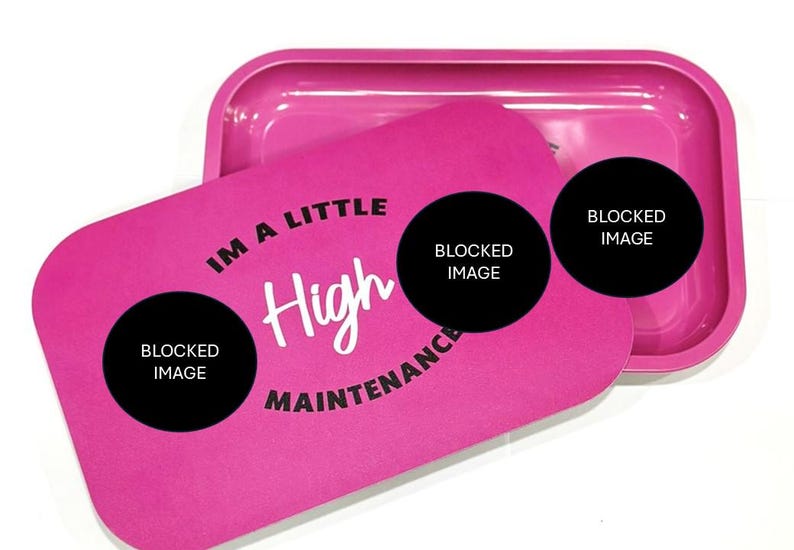May include: Pink rolling tray with a black lid. The lid has the text "I'm a little high maintenance" with a black circle around the text. There are three black circles with the text "Blocked Image" inside each circle.