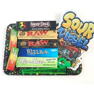 May include: A green rolling tray with a green plastic poker and various rolling papers, including Wise Skies, Raw, and Rizla+. A sticker with the words "Sour Diesel" is on the tray.