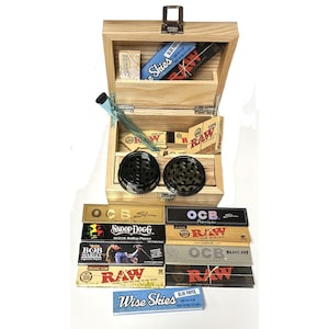 May include: A wooden box with a hinged lid, containing various rolling papers, a grinder, and a glass pipe. The box is filled with different brands of rolling papers, including RAW, OCB, and Wise Skies. The box is a great way to store and organise your smoking supplies.