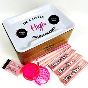 Puede incluir: Una bandeja de rodadura de madera con una tapa blanca que dice "Soy un poco de alto mantenimiento". La bandeja tiene un peque&ntilde;o compartimento para papeles de fumar y un molinillo. Tambi&eacute;n hay papeles de fumar rosas y molinillos rosas en la imagen.