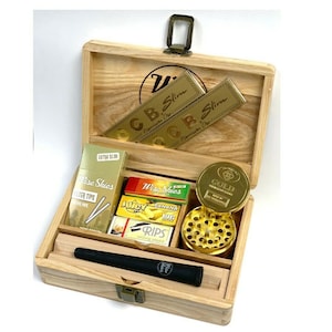 May include: A wooden box set containing various smoking accessories. Includes gold rolling papers, a grinder, filter tips, and rolling papers. The box has a hinged lid and a metal clasp. The set is designed for convenience and portability.