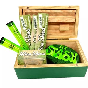 May include: A wooden box with a green lid, containing a green rock with the words "My Stash" on it, three green rolling papers with the words "Wise Skies Green Hemp" on them, and two green tubes with the words "Wise Skies" on them.