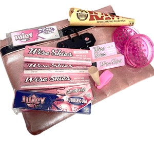 May include: A pink zippered pouch with a combination lock, containing various rolling papers, a grinder, and a cone. The rolling papers include Juicy Jays, Wise Skies, and RAW. The grinder is pink and has a clear lid. The cone is brown and has a pink tip.