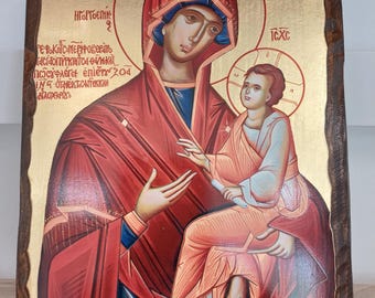 May include: A religious icon depicting a woman and child, painted on a wooden plaque. The woman wears a red head covering and robe, with a blue undergarment. The child is in a similar style, with a halo. Gold background and text.