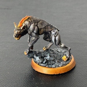 Może przedstawiać: Pomalowana na czarno i srebrno miniatura stworzenia przypominającego wilka, które warczy i ma pomarańczowe płomienie na grzbiecie. Stworzenie stoi na czarno-szarej podstawie skalnej z miedzianą obwódką.