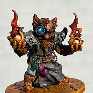 May include: A painted miniature figurine of a dwarf wizard holding two glowing orbs in his hands. He is wearing a brown leather vest, a grey robe, and a pair of goggles with a blue lens.