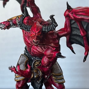 Può includere: Una figura di demone in miniatura dipinta di rosso e nero con ali, corna e una spada. La figura è in una posa dinamica, con le ali spiegate e la spada alzata.