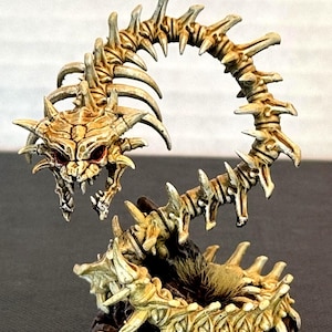 May include: A detailed, hand-painted fantasy miniature of a skeletal worm-like creature. The figure features a bone-colored body with sharp, spiky protrusions and a menacing skull-like head with red eyes. The base is dark and textured.