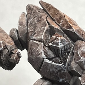 Pode incluir: Um close-up de uma figura de golem de pedra cinza, marrom e branca. O golem &eacute; feito de muitas pe&ccedil;as de pedra diferentes e tem uma superf&iacute;cie &aacute;spera e texturizada.