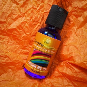 May include: A blue bottle of hand sanitizer with a rainbow design and the text "Cheer Me Up!"  Everyday Intentions Essential Oil Blends.  Hydrating Hand Sanitizer 1 fl. oz (30ml).