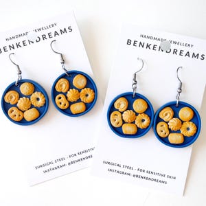 May include: Handmade earrings with a blue circular base, adorned with miniature cookie designs. The earrings have silver-coloured hooks and are presented on white cards with the text "BENKENDREAMS". Made from surgical steel for sensitive skin.