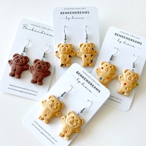 May include: Four pairs of handmade cookie bear earrings. The earrings are made of polymer clay and feature different coloured glazes. The earrings are on white cards with the text "Benkendreams by diana" printed on them.