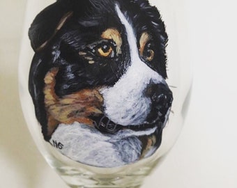 Könnte beinhalten: Handbemaltes Weinglas mit einem Nahaufnahmeporträt eines schwarz-braun-weißen Hundes mit weißer Schnauze. Die Augen des Hundes sind braun und das Glas ist klar.